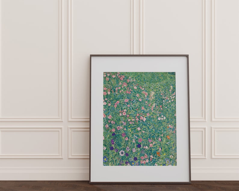 Op de afbeelding: Een ingelijste print van een schilderij dat een veld met bloemen in tinten roze, wit en paars toont. De bloemen worden omringd door groen gebladerte en de achtergrond is lichtblauw.