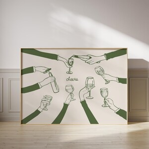 May include: A framed print featuring a green line drawing of hands toasting with wine glasses and bottles. The word "cheers" is written in cursive. The artwork is set against a cream-colored background.