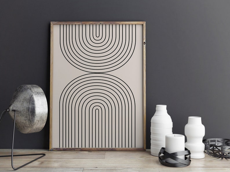 May include: A framed print with a minimalist geometric design featuring black arches on a beige background. The print is displayed on a wooden surface with white vases and candles.