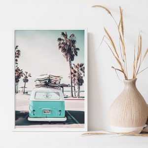 May include: A vintage teal blue van with surfboards on the roof parked on a beach with palm trees in the background.
