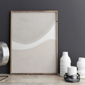 May include: A framed abstract print with beige and white watercolour-like shapes hangs on a dark grey wall.  A silver lamp, two white ceramic vases, and a black candle holder with a white candle are on a wooden table in front of the print.