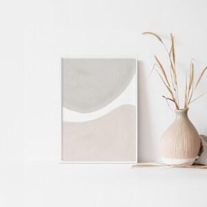 May include: A framed abstract print with a white background and two overlapping shapes in shades of grey and beige.