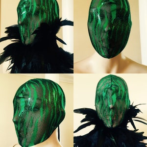 May include: Green and black masquerade mask with a zebra print pattern. The mask is made of a sheer fabric and has a black feather boa around the neck.