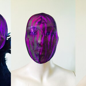 May include: A black mesh head covering with a pink and purple paint splatter design. The head covering has a black ribbon tie at the back.