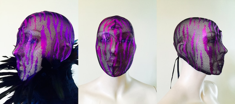 May include: A black mesh head covering with a pink and purple paint splatter design. The head covering has a black ribbon tie at the back.