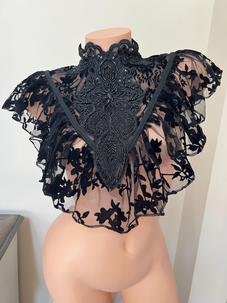 May include: Black lace choker with a beaded floral design. The choker has a high collar and a ruffled edge.