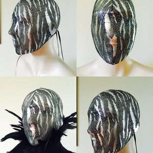 May include: A black and white zebra patterned mesh mask with a black ribbon tie. The mask is on a white mannequin head.
