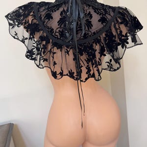 May include: Black lace choker with a ruffled edge and a lace-up back. The choker is made of a sheer fabric with a floral pattern.