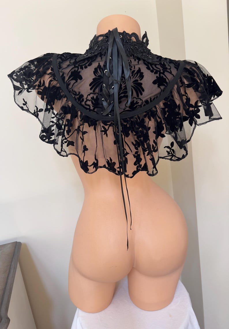 May include: Black lace choker with a ruffled edge and a lace-up back. The choker is made of a sheer fabric with a floral pattern.