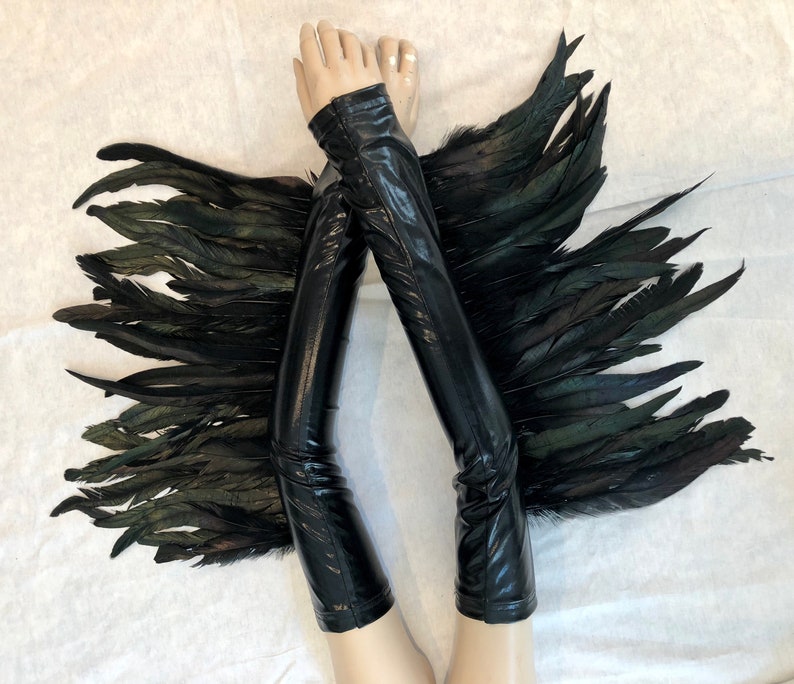 May include: A pair of black leather arm warmers with black feather wings attached. The arm warmers are long and reach to the elbow. The feathers are soft and fluffy.