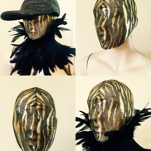 May include: A gold and black zebra-print mask with a black feather boa collar. The mask is on a mannequin head.
