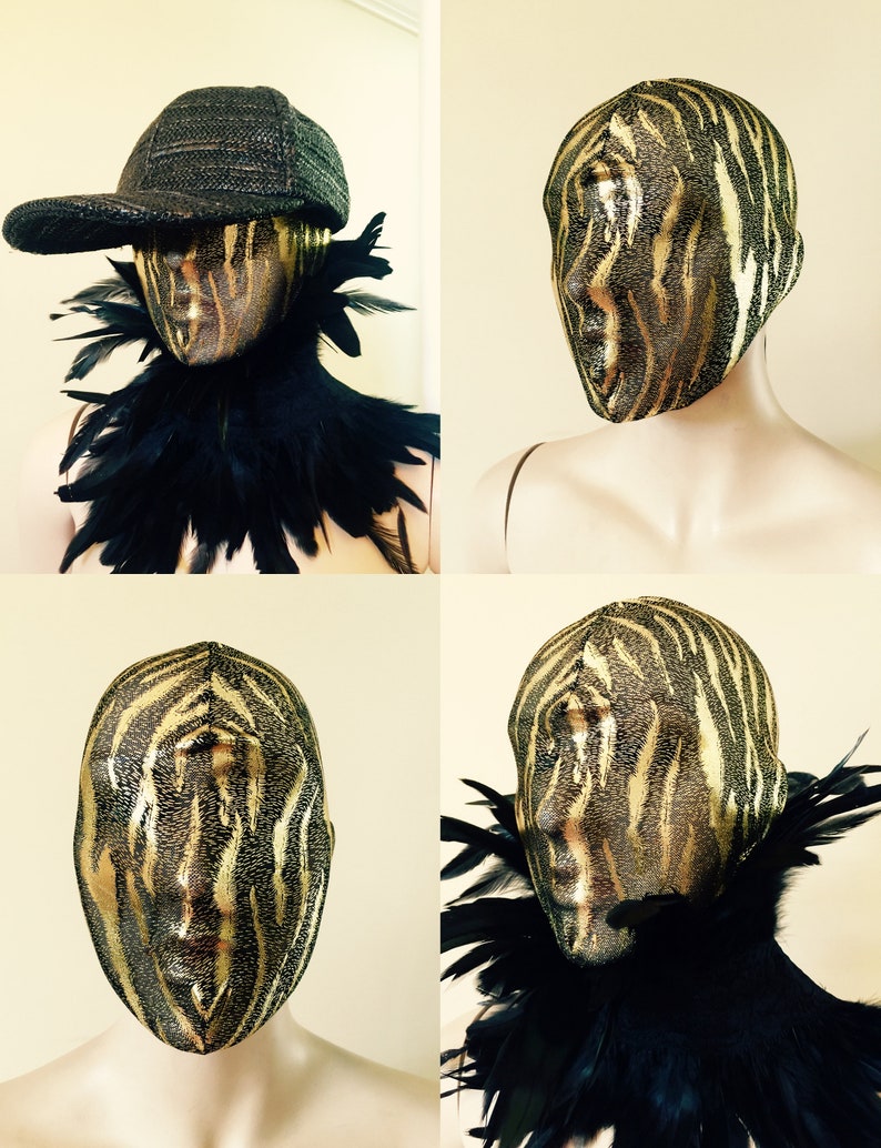 May include: A gold and black zebra-print mask with a black feather boa collar. The mask is on a mannequin head.