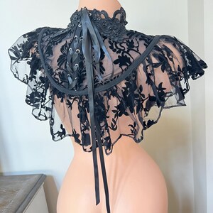 May include: Black lace choker with a ruffled edge and a satin ribbon tie. The choker features a floral pattern and is embellished with small black beads.