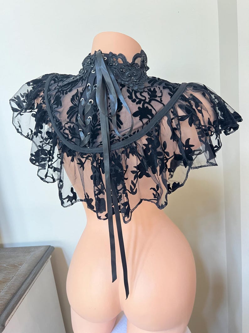 May include: Black lace choker with a ruffled edge and a satin ribbon tie. The choker features a floral pattern and is embellished with small black beads.