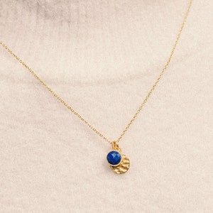 May include: A gold chain necklace with a small pendant featuring a blue gemstone and a textured gold disc.
