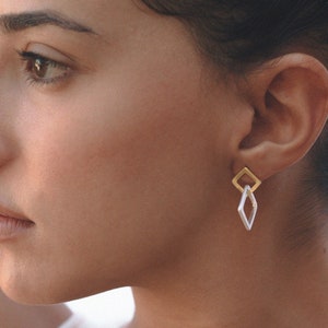 May include: A woman wearing a white tank top with gold and silver geometric earrings.
