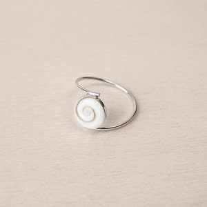 Puede incluir: Un anillo de plata con una incrustación de concha blanca con un patrón en espiral.