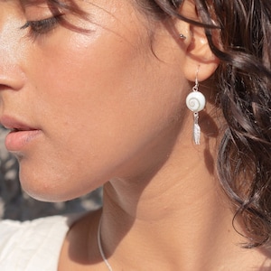 Könnte beinhalten: Eine silberne Halskette mit einem weißen Muschelanhänger und einem passenden Paar Ohrringe mit weißen Muschel-Tropfen. Die Halskette und die Ohrringe haben eine zarte silberne Kette.