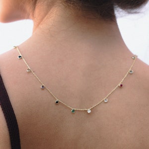 May include: A gold chain necklace with small colourful gemstones hanging from it. The necklace is worn by a person with brown skin.