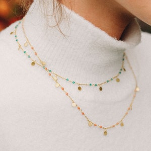 May include: A gold necklace with two strands of small beads, one strand is coral colored and the other is green.  The necklace has small gold discs hanging from it.