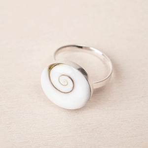 Puede incluir: Un anillo de plata con una incrustación de concha blanca con un patrón en espiral.