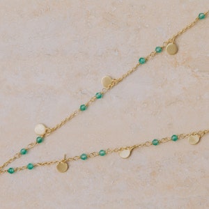 May include: A gold necklace with green beads and small gold discs hanging from it.