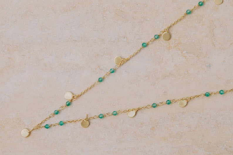 May include: A gold necklace with green beads and small gold discs hanging from it.