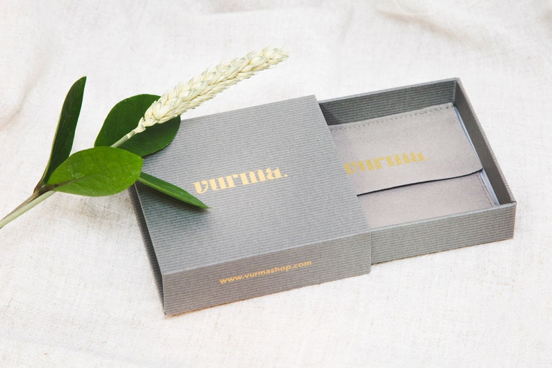 May include: A gray gift box with a gold logo that reads "remarkable." The box is open, revealing a gray velvet pouch with the same gold logo. The box is sitting on a white fabric surface.