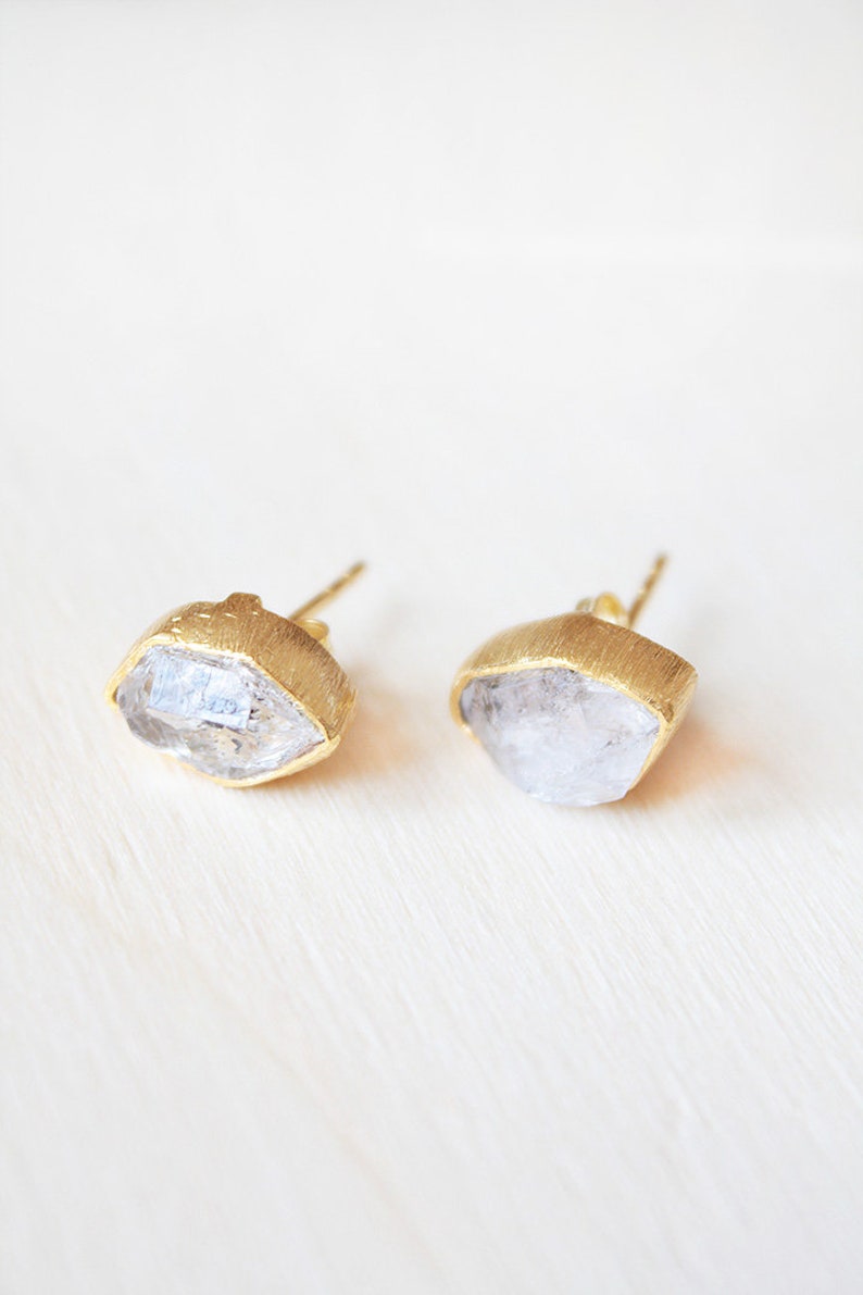 May include: A pair of gold earrings with clear quartz stones. The stones are faceted and have a rough, natural look.
