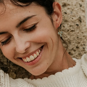 May include: A close-up of a woman smiling with her eyes closed. She is wearing gold earrings with light blue gemstone accents.