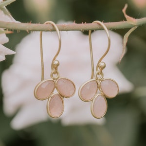 May include: A pair of gold earrings with pink gemstone drops. Each earring features three teardrop-shaped stones.