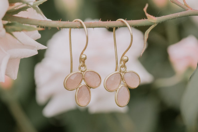 May include: A pair of gold earrings with pink gemstone drops. Each earring features three teardrop-shaped stones.
