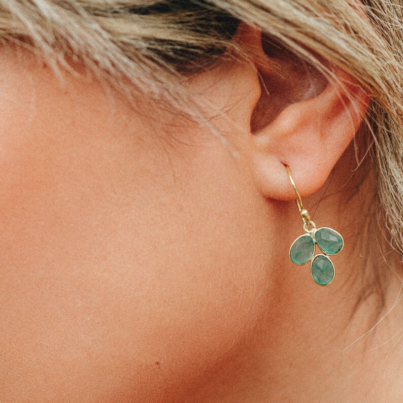 May include: Gold dangle earrings with a cluster of three teardrop-shaped green gemstones.