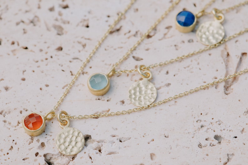 May include: Three gold necklaces with different colored gemstones and hammered gold disc pendants. The necklaces feature a light blue, a dark blue, and an orange gemstone.