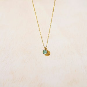 May include: A gold chain necklace with a small, round, light blue gemstone pendant and a hammered gold disc pendant.