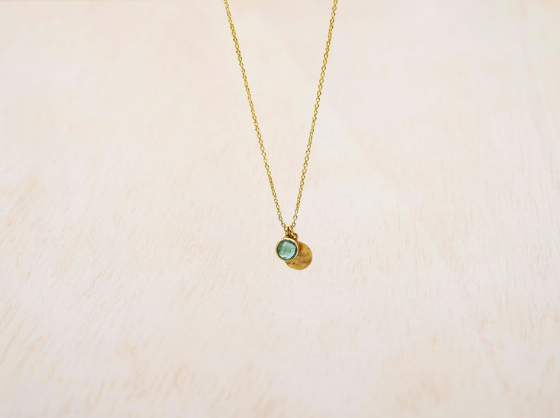 May include: A gold chain necklace with a small, round, light blue gemstone pendant and a hammered gold disc pendant.
