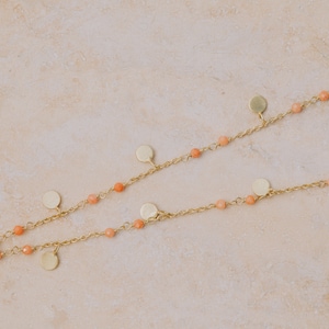 May include: A gold chain necklace with small, round, peach-colored beads and gold disc charms.