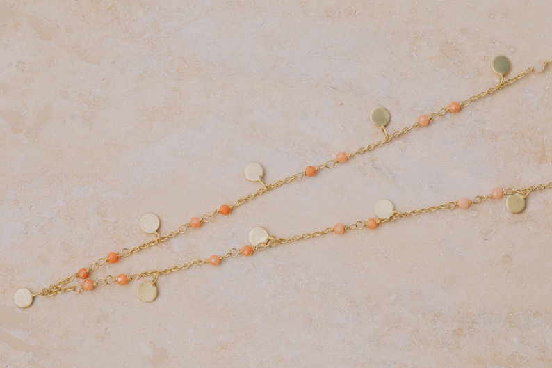 May include: A gold chain necklace with small, round, peach-colored beads and gold disc charms.