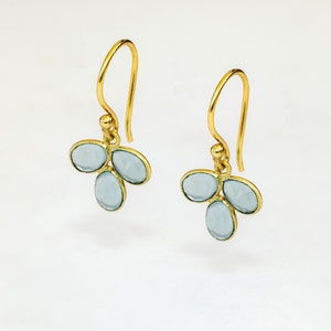 May include: A pair of gold dangle earrings with three light blue oval-shaped gemstones on each earring.