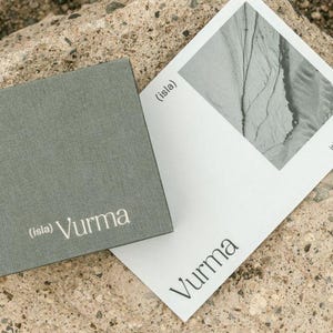 May include: A gray textured box with the text "(isla) Vurma" printed in white. A white card with the text "(isla) Vurma" and the website "isleavurma.com" printed in black. The card has a black and white image of a rocky landscape.
