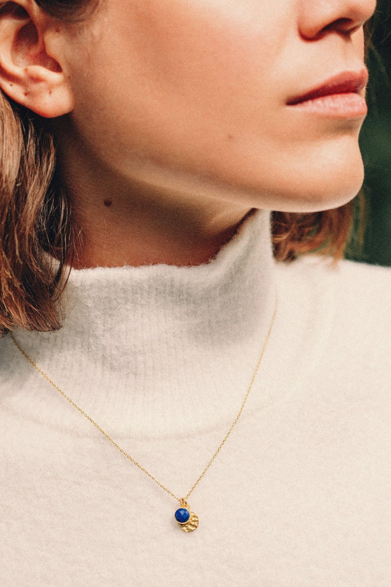 May include: A gold chain necklace with a small pendant featuring a blue gemstone and a textured gold disc.