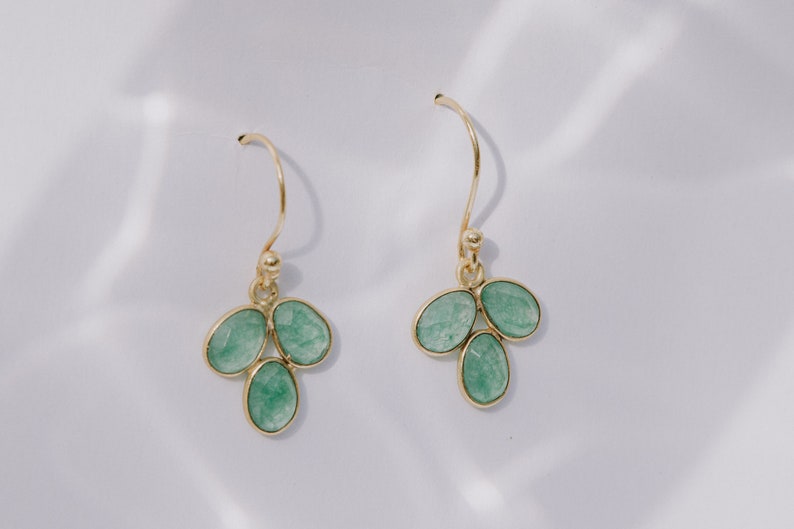 May include: A pair of gold dangle earrings with three green gemstone drops each.