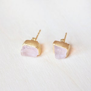 May include: A pair of gold earrings with pink quartz stones. The stones are irregular in shape and have a natural, raw look.