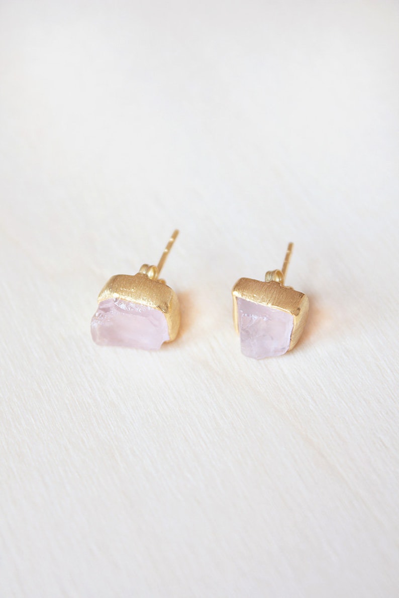 May include: A pair of gold earrings with pink quartz stones. The stones are irregular in shape and have a natural, raw look.