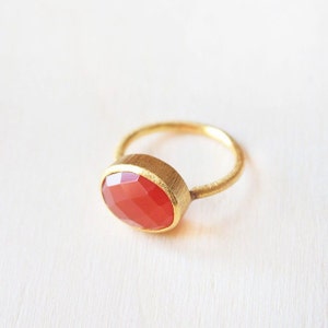 May include: A gold ring featuring a red carnelian gemstone. The ring has a simple, elegant design.