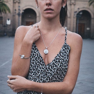 Puede incluir: Un conjunto de collar con colgante, pulsera y pendientes de plata. El colgante y la pulsera presentan un dise&ntilde;o en espiral. La modelo lleva un vestido con estampado floral en blanco y negro. Un accesorio delicado.