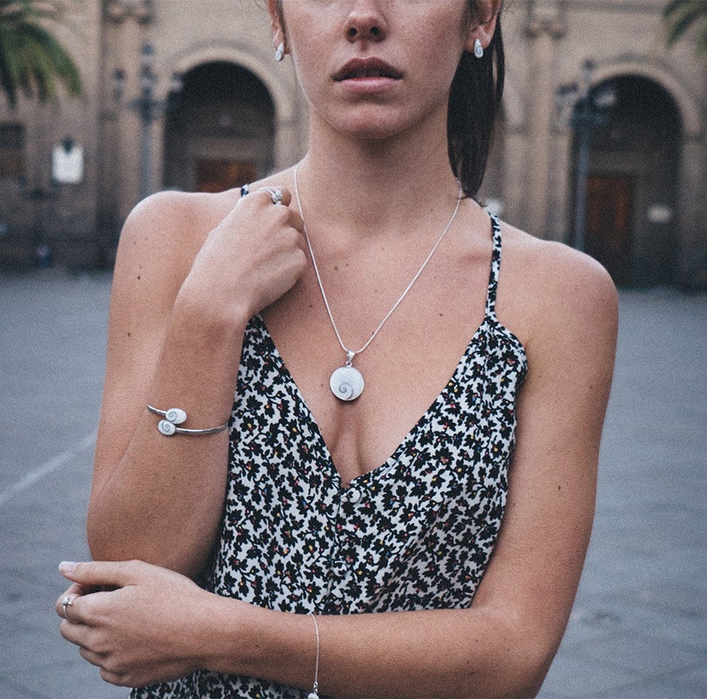 Puede incluir: Un conjunto de collar con colgante, pulsera y pendientes de plata. El colgante y la pulsera presentan un dise&ntilde;o en espiral. La modelo lleva un vestido con estampado floral en blanco y negro. Un accesorio delicado.