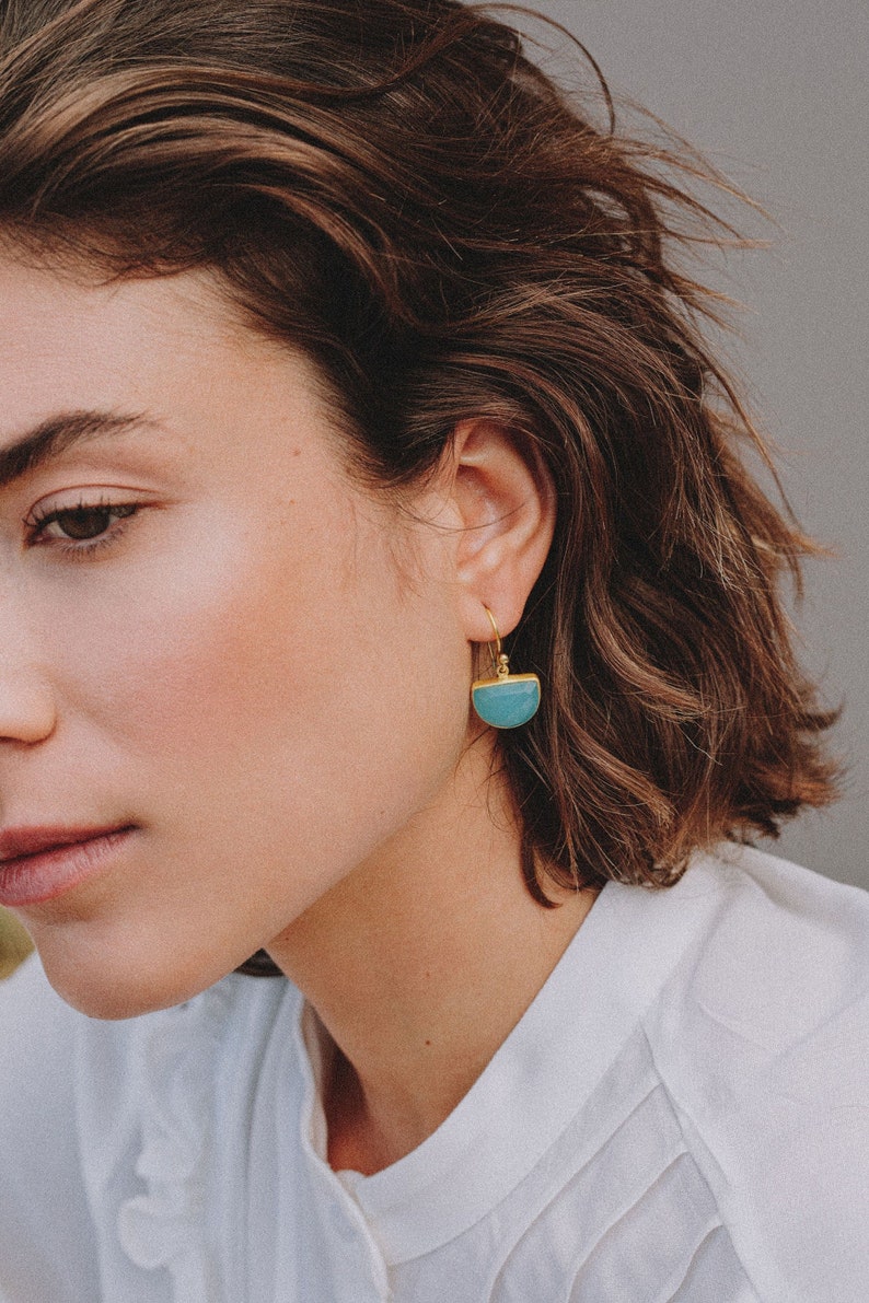 Earrings half circumference shaped with a natural gemstone aqua chalcedony. They are hanging by a hook closing on the ear of a model with mid long haircut.