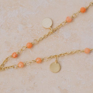 May include: A gold chain necklace with small orange beads and round gold charms.