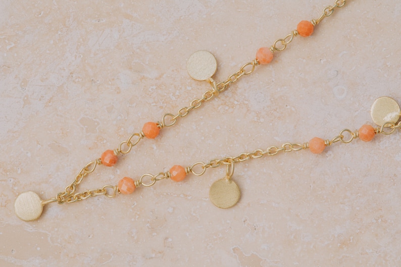May include: A gold chain necklace with small orange beads and round gold charms.